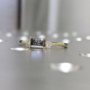 May include: A gold ring with a rectangular grey diamond and two smaller diamonds on the band.