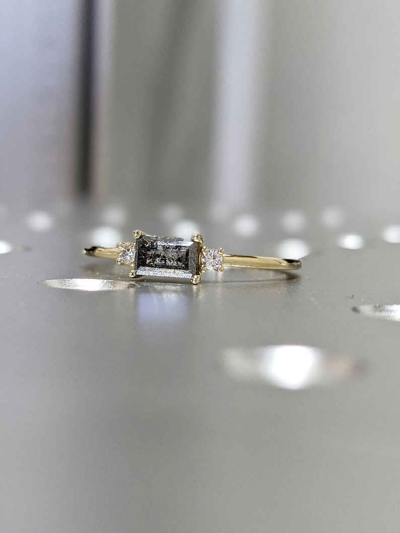 May include: A gold ring with a rectangular grey diamond and two smaller diamonds on the band.