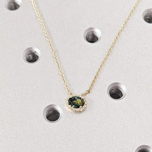 May include: A gold chain necklace with a green oval gemstone pendant surrounded by a halo of smaller diamonds.