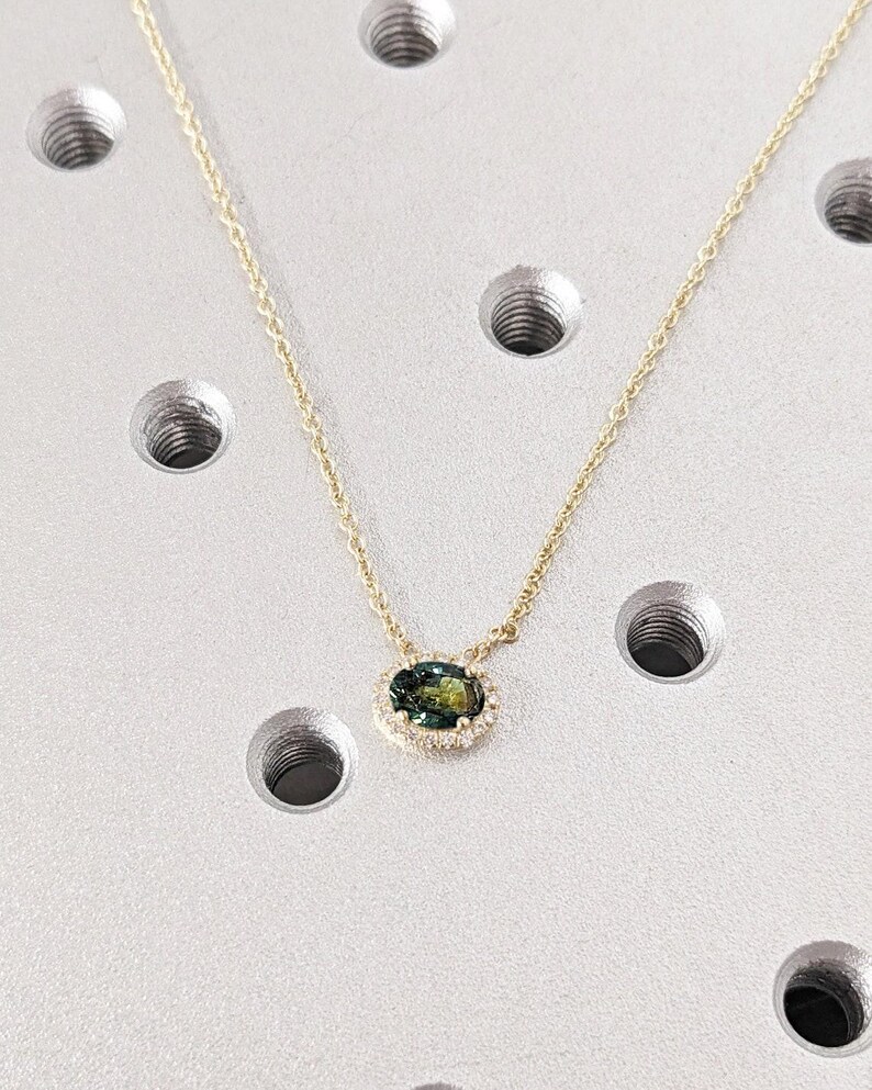 May include: A gold chain necklace with a green oval gemstone pendant surrounded by a halo of smaller diamonds.