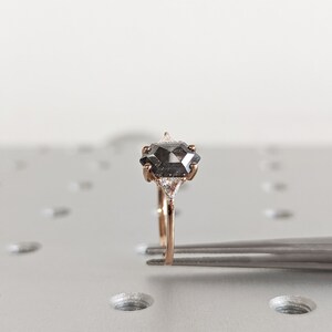 May include: A rose gold ring with a black diamond center stone and two smaller diamonds on either side.
