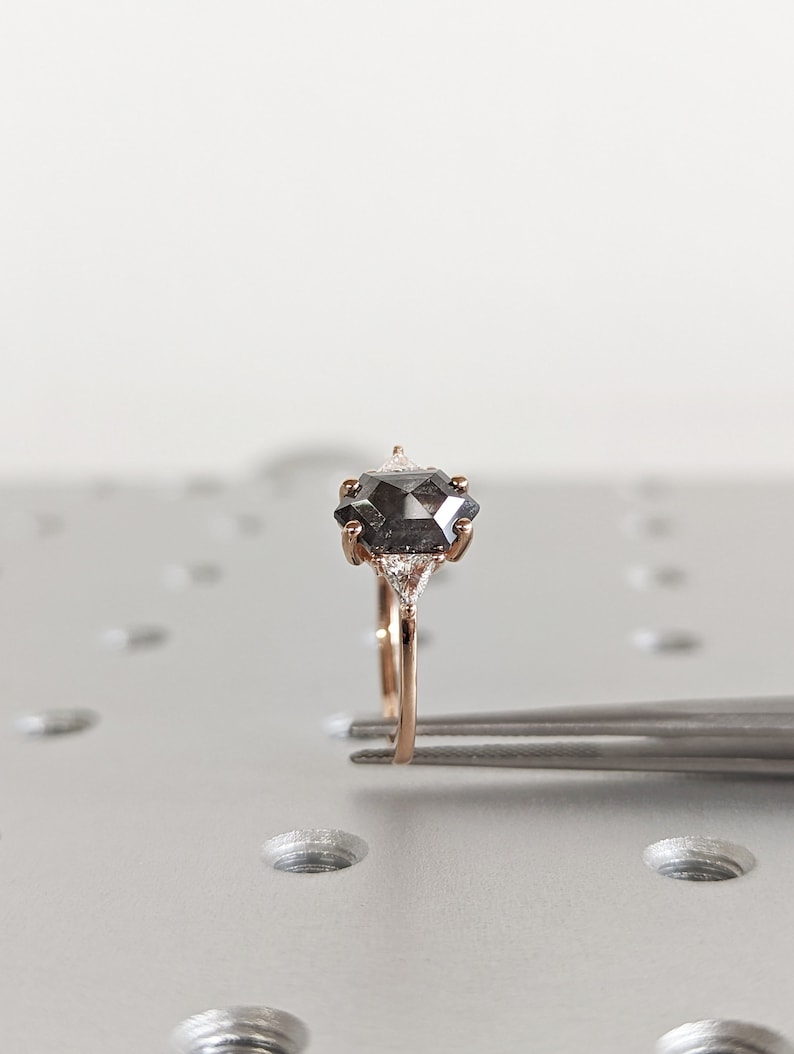 May include: A rose gold ring with a black diamond center stone and two smaller diamonds on either side.
