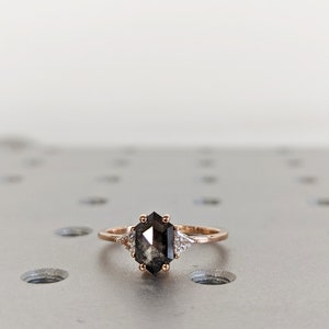 May include: A rose gold ring with a black hexagonal diamond and two smaller white diamonds on the band.