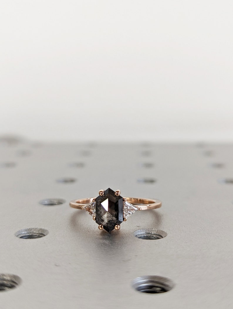 May include: A rose gold ring with a black hexagonal diamond and two smaller white diamonds on the band.
