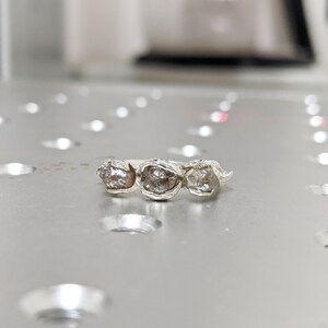 以下が含まれることがあります： 3つの粗い、透明でグレーのダイヤモンドがバンドにセットされたシルバーリング