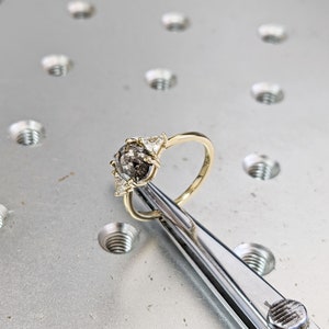Puede incluir: Un anillo de oro con una piedra preciosa gris y blanca rodeada de tres piedras blancas m&aacute;s peque&ntilde;as.