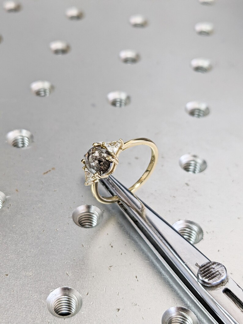 Puede incluir: Un anillo de oro con una piedra preciosa gris y blanca rodeada de tres piedras blancas m&aacute;s peque&ntilde;as.