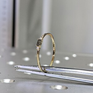 May include: A delicate gold band ring with a small rectangular black diamond and two smaller diamonds on either side.