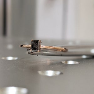 May include: A delicate gold ring with a square-shaped black gemstone.