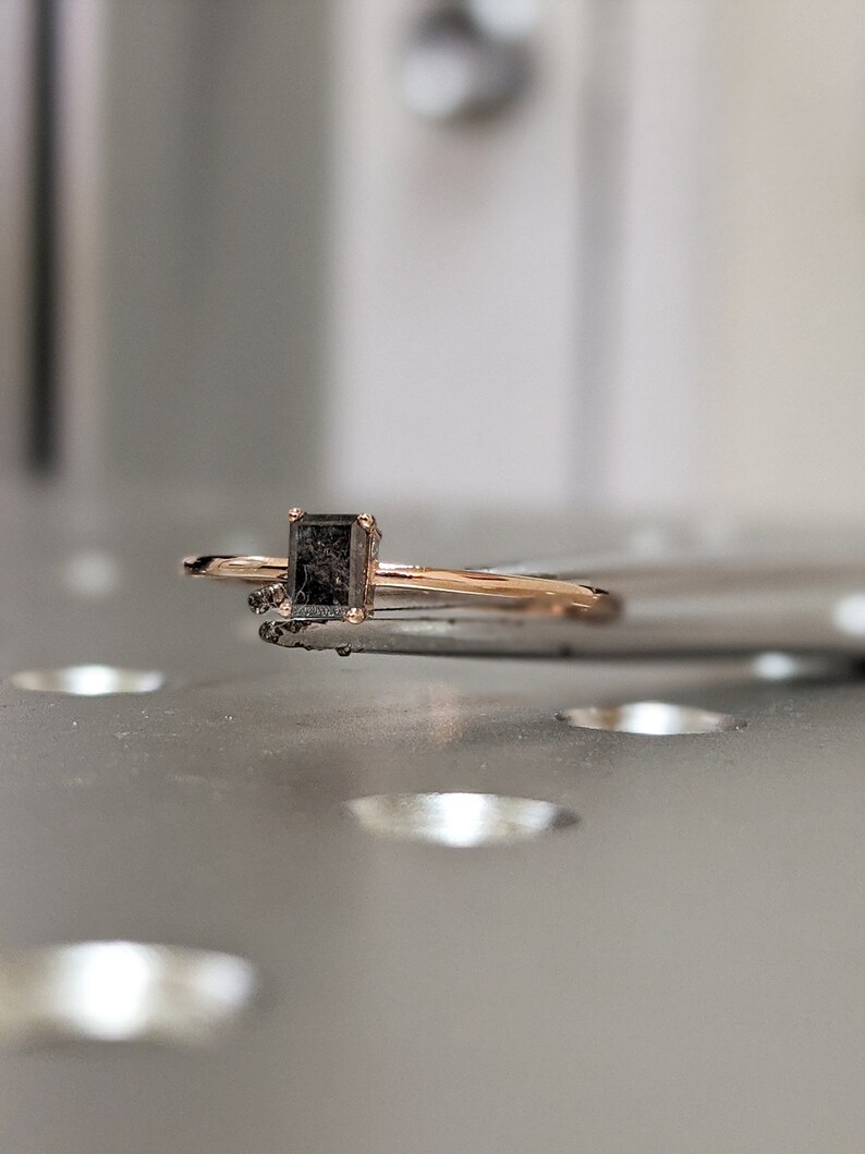May include: A delicate gold ring with a square-shaped black gemstone.
