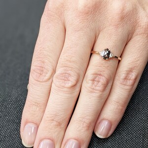 May include: A rose gold engagement ring with a black diamond and two smaller diamonds on the band.