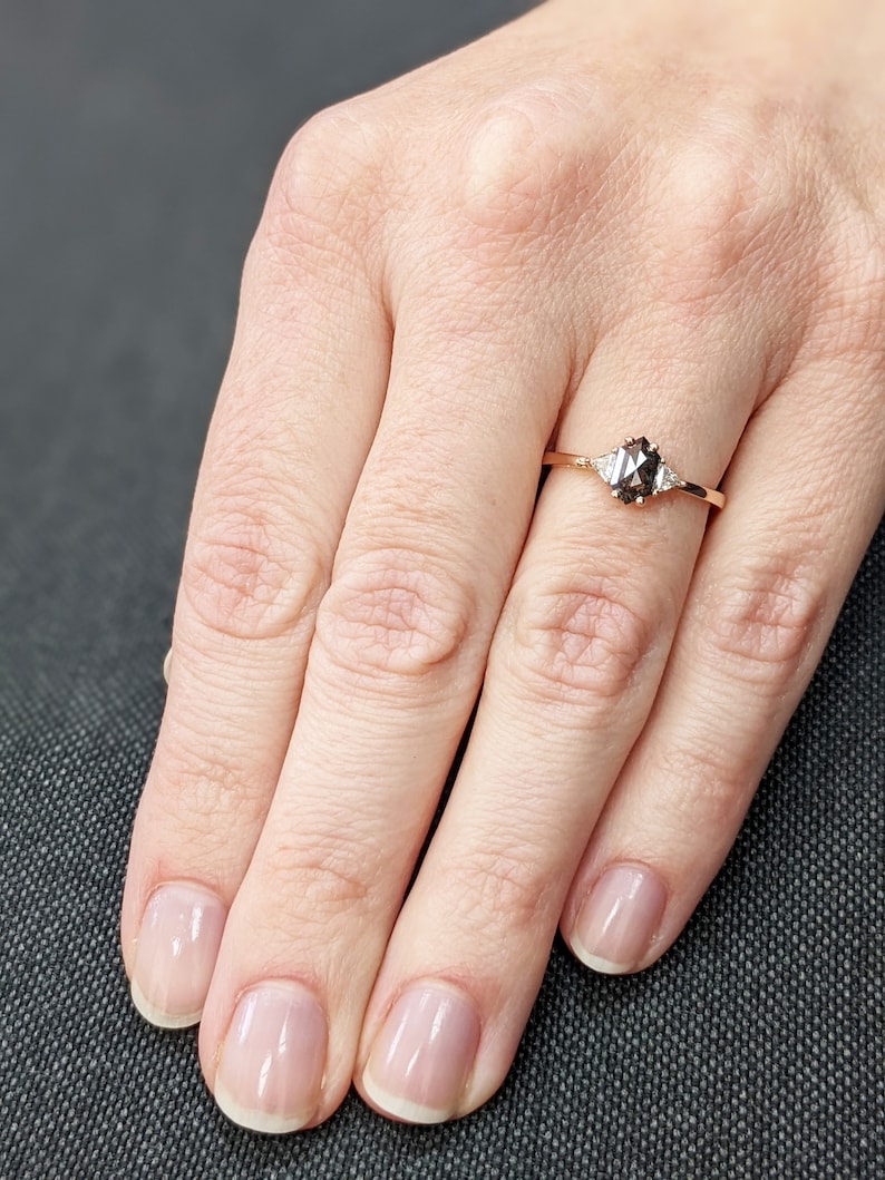 May include: A rose gold engagement ring with a black diamond and two smaller diamonds on the band.