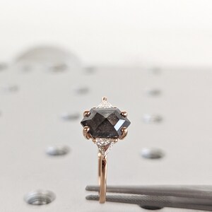 May include: A rose gold ring with a black octagonal diamond and two smaller white diamonds on the band.