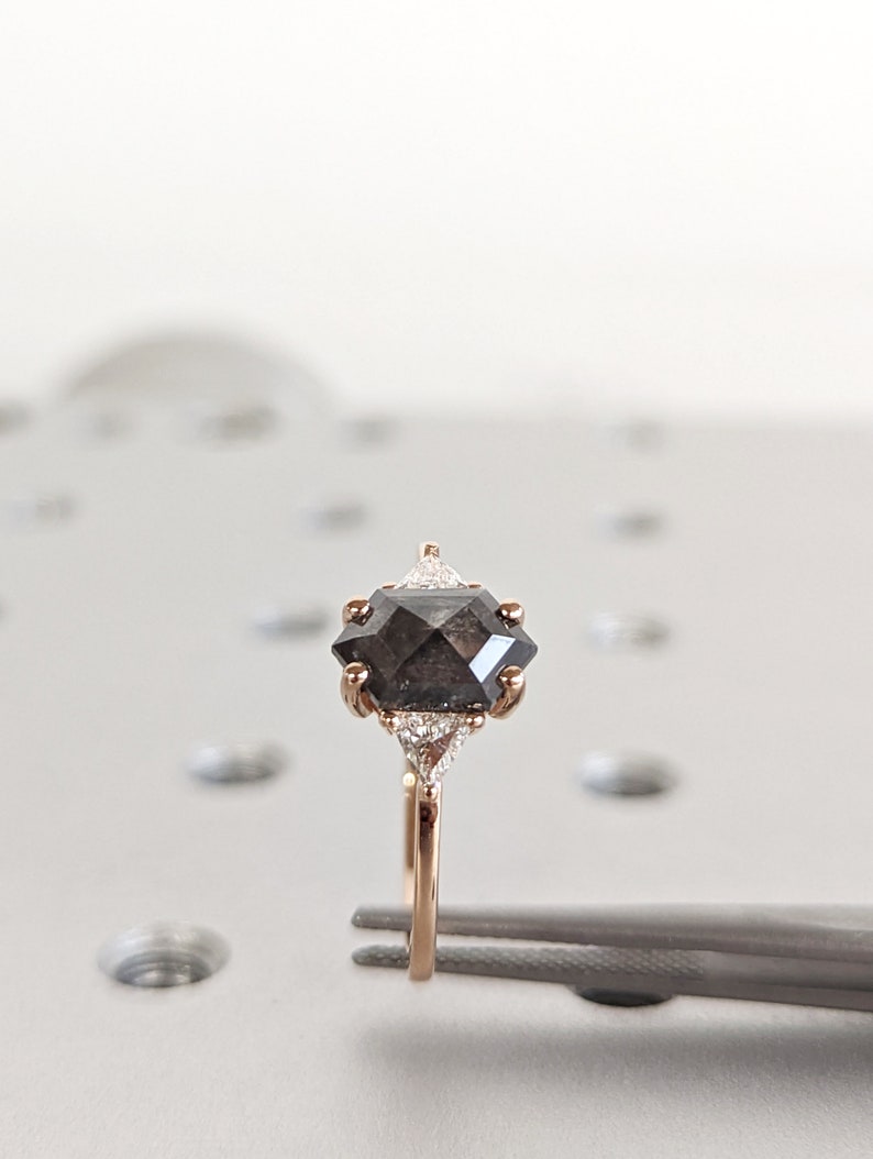 May include: A rose gold ring with a black octagonal diamond and two smaller white diamonds on the band.