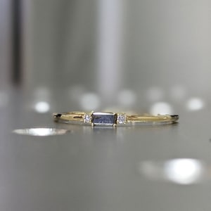 May include: A delicate gold band ring with a rectangular grey gemstone and two smaller clear gemstones on either side.