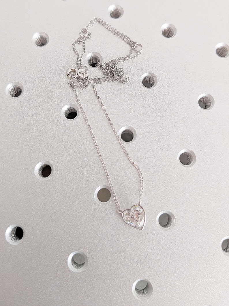 Puede incluir: Un collar de cadena de plata con un colgante en forma de coraz&oacute;n con una piedra transparente y brillante.
