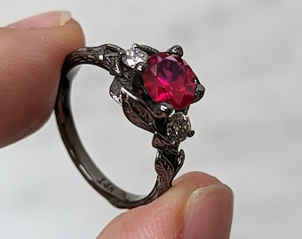 May include: Black ring with a red gemstone and two smaller white gemstones set in a leaf design. The ring is marked "14K".