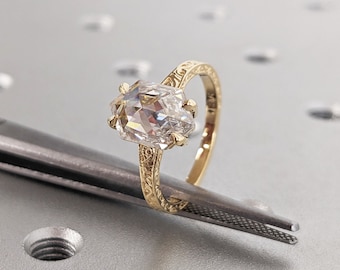 May include: A gold engagement ring featuring a large, clear, faceted gemstone. The ring has a delicate, ornate design on the band.