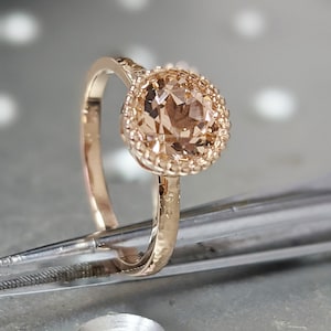 Può includere: Un anello in oro rosa con una fascia testurizzata e una pietra preziosa rotonda di colore marrone chiaro incastonata a bezel.