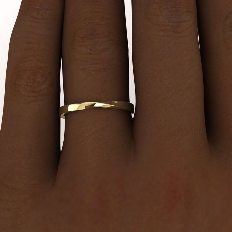 May include: A simple gold band ring with a twisted design. The ring is worn on a finger.