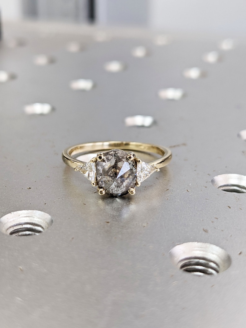Puede incluir: Un anillo de oro con una piedra preciosa ovalada gris y dos diamantes triangulares m&aacute;s peque&ntilde;os a cada lado.