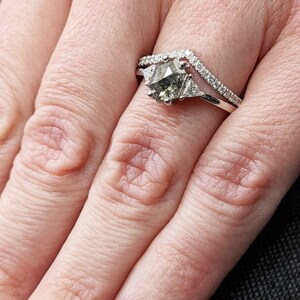 May include: A silver ring with a large, gray, faceted gemstone surrounded by smaller diamonds. The ring is set on a finger with a white nail polish.