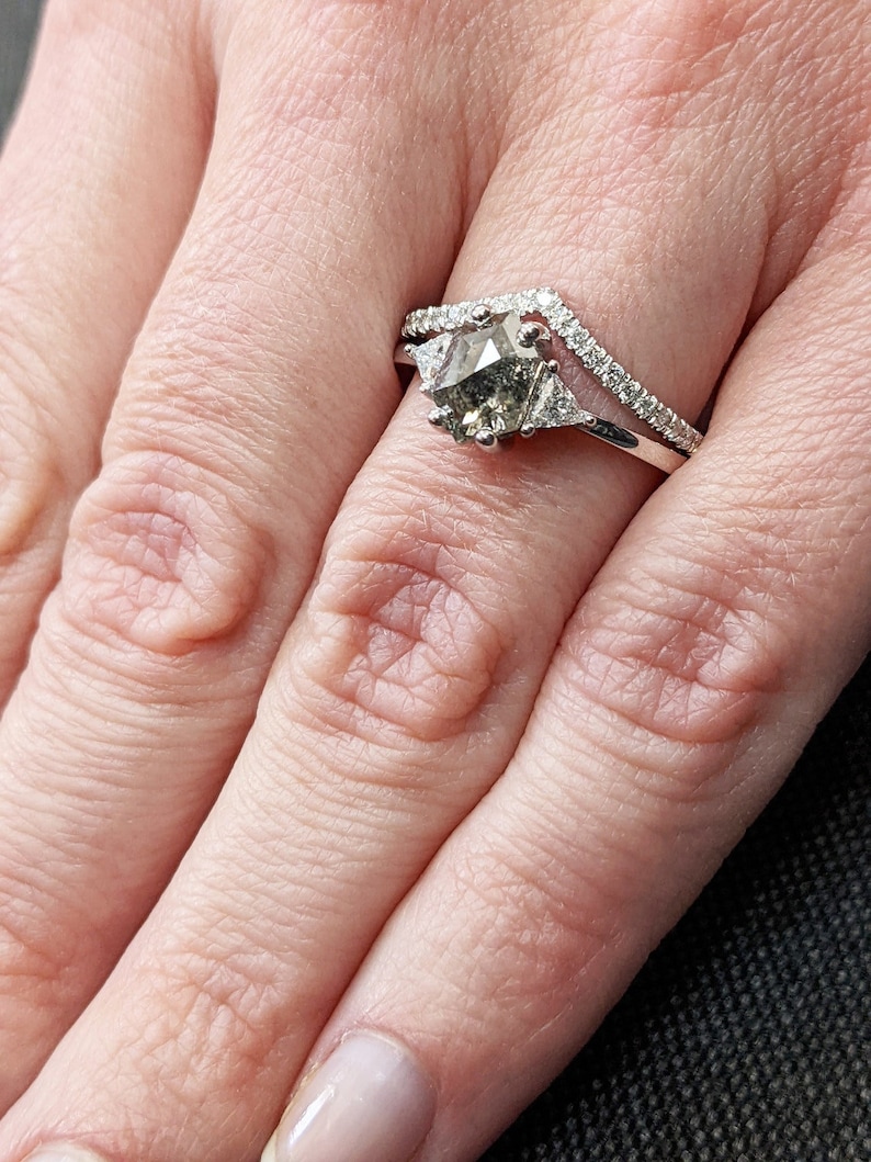 May include: A silver ring with a large, gray, faceted gemstone surrounded by smaller diamonds. The ring is set on a finger with a white nail polish.