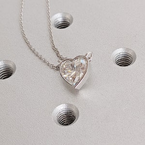 Puede incluir: Un collar de cadena de plata con un colgante en forma de coraz&oacute;n que presenta una gran piedra preciosa facetada transparente.