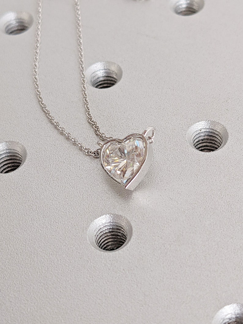 Puede incluir: Un collar de cadena de plata con un colgante en forma de coraz&oacute;n que presenta una gran piedra preciosa facetada transparente.