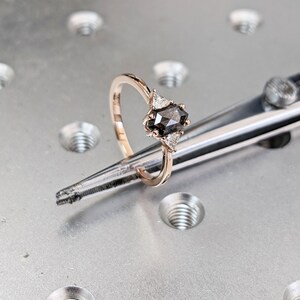 May include: A rose gold engagement ring with a black diamond center stone and three smaller white diamonds on the band.