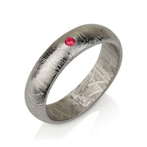 Könnte beinhalten: Ein silberner Ring mit einem roten Edelstein in der Mitte. Der Ring ist aus Meteoritenmetall gefertigt und hat eine einzigartige, strukturierte Oberfläche.