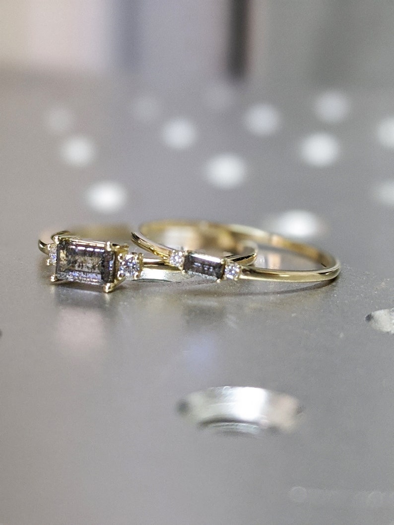 May include: Two gold rings with a grey rectangular stone and small diamonds on the band.