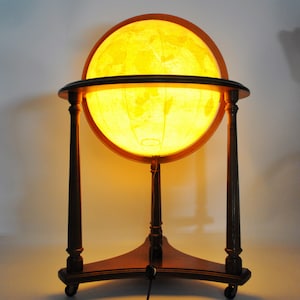 May include: A wooden globe stand with a lit globe. The globe is illuminated from within, casting a warm glow. The stand has a triangular base and three pillars supporting the globe.