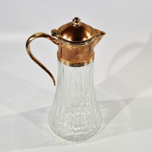 May include: A clear glass pitcher with a ribbed design and a gold-toned metal lid. The lid has a copper-toned top.