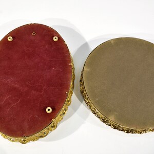 Puede incluir: Dos bandejas decorativas de forma ovalada con marcos de metal dorado. La bandeja superior tiene un forro de terciopelo rojo y la bandeja inferior tiene un forro de fieltro marr&oacute;n.