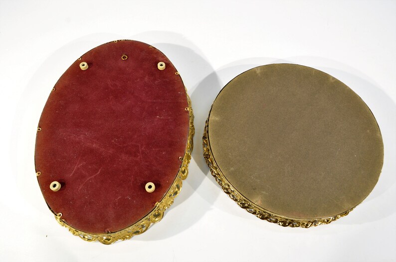 Puede incluir: Dos bandejas decorativas de forma ovalada con marcos de metal dorado. La bandeja superior tiene un forro de terciopelo rojo y la bandeja inferior tiene un forro de fieltro marr&oacute;n.