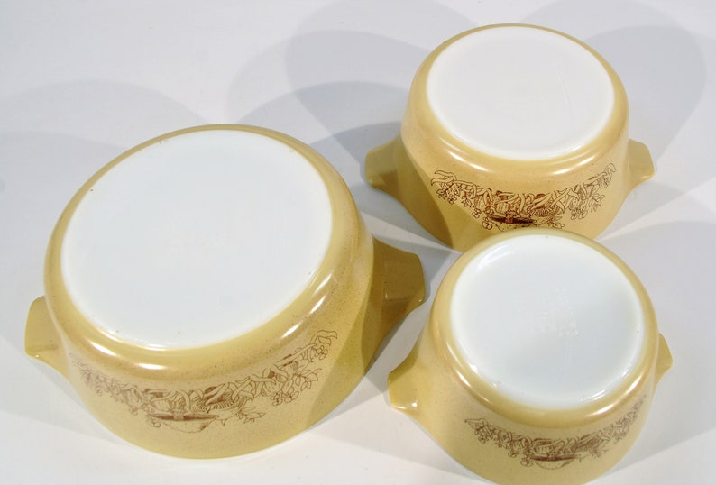 K&ouml;nnte beinhalten: Set aus drei gelben Auflaufformen mit braunen Blumendesigns und wei&szlig;en Innenr&auml;umen. Die Formen haben jeweils zwei Griffe.