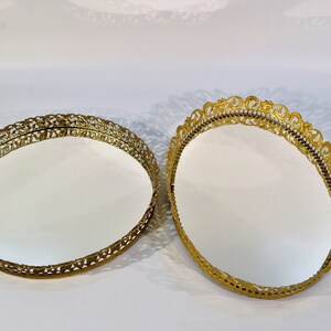 Puede incluir: Dos bandejas redondas decorativas de color dorado con bordes adornados con filigranas. Las bandejas tienen una superficie de espejo.