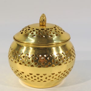 May include: A gold metal container with a decorative, intricate, cut-out design. The container has a lid with a small knob on top.