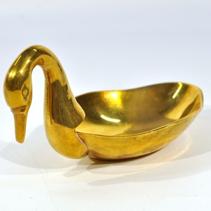 May include: A gold-colored swan-shaped trinket dish. The dish is made of metal and has a smooth, shiny surface.