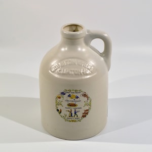 May include: A white ceramic pitcher with a handle. It has a circular design with the text "First the Toast Then the Roast Happy Hostess Happy Host" in a wreath of flowers and other designs.