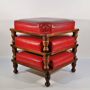 May include: A red upholstered ottoman with a wooden frame and turned legs. The ottoman is stacked on top of two other ottomans, creating a tiered effect.