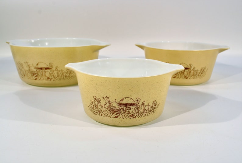 K&ouml;nnte beinhalten: Set aus drei gelben Pyrex-Sch&uuml;sseln mit einem braunen Pilz- und Blumendesign.