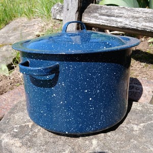 May include: A deep, cylindrical stockpot with a matching lid, featuring a dark blue enamel finish with a white speckled pattern. The pot includes two side handles and a small loop handle on the lid, constructed from durable metal material.