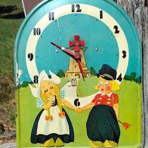 May include: Vintage wall clock with a teal face and a whimsical illustration. The clock features a windmill and two children in traditional Dutch attire. The clock hands are red, and the numbers are black.