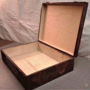 May include: A large, rectangular wooden box with an open hinged lid. The exterior features a dark, textured finish with a subtle floral pattern in shades of brown and black. The interior is lined with light, unfinished natural wood panels.