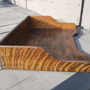 May include: A vintage wooden tray with a dark brown finish and a unique grain pattern. The tray has a rectangular shape with curved edges and a raised lip, perfect for organizing items. The wood has a warm, inviting tone.