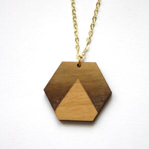 May include: A gold chain necklace with a hexagonal pendant made of two different types of wood. The pendant has a geometric design with a light brown triangle in the center.