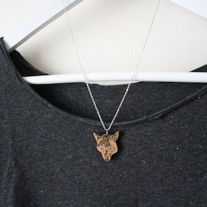 May include: A silver chain necklace with a wooden fox pendant. The pendant is detailed with intricate carvings and has a natural wood finish.