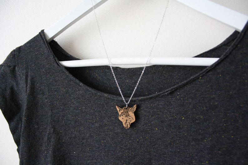 May include: A silver chain necklace with a wooden fox pendant. The pendant is detailed with intricate carvings and has a natural wood finish.
